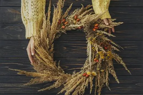 Woman holds wreath made of pampas grass and dried flowers in her hands